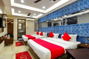 A hotel room with two beds, red and white bedding, a blue headboard, a mirror, a wardrobe, a vanity, and a ceiling fan. - Hotel Vanson Delite (New Delhi)