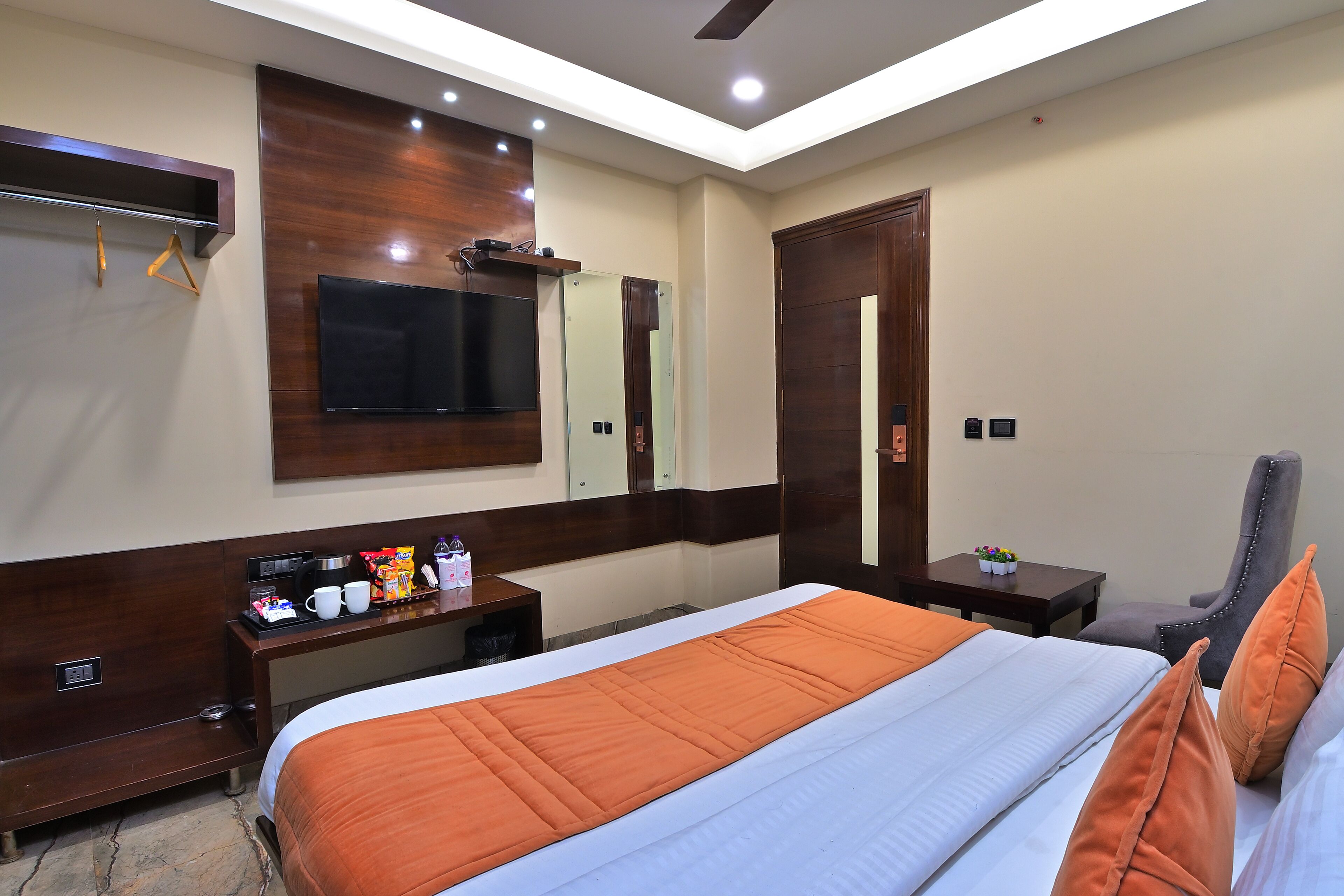 A hotel room with a large bed, a desk with a flat-screen TV, a mirror, and a wardrobe.