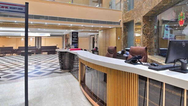 A hotel reception area with a check-in counter, seating area, and a security check sign. - Hotel Vanson Delite (New Delhi)