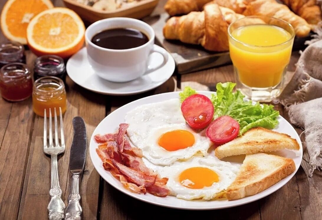 Un plato de desayuno con huevos, tocino, tostadas y tomates sobre una mesa de madera.