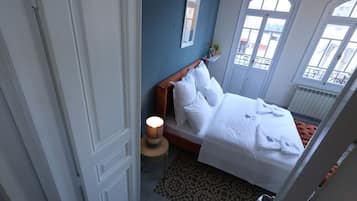Habitación de hotel con cama, mesita de noche con lámpara, alfombra estampada y vistas al exterior a través de amplias ventanas.