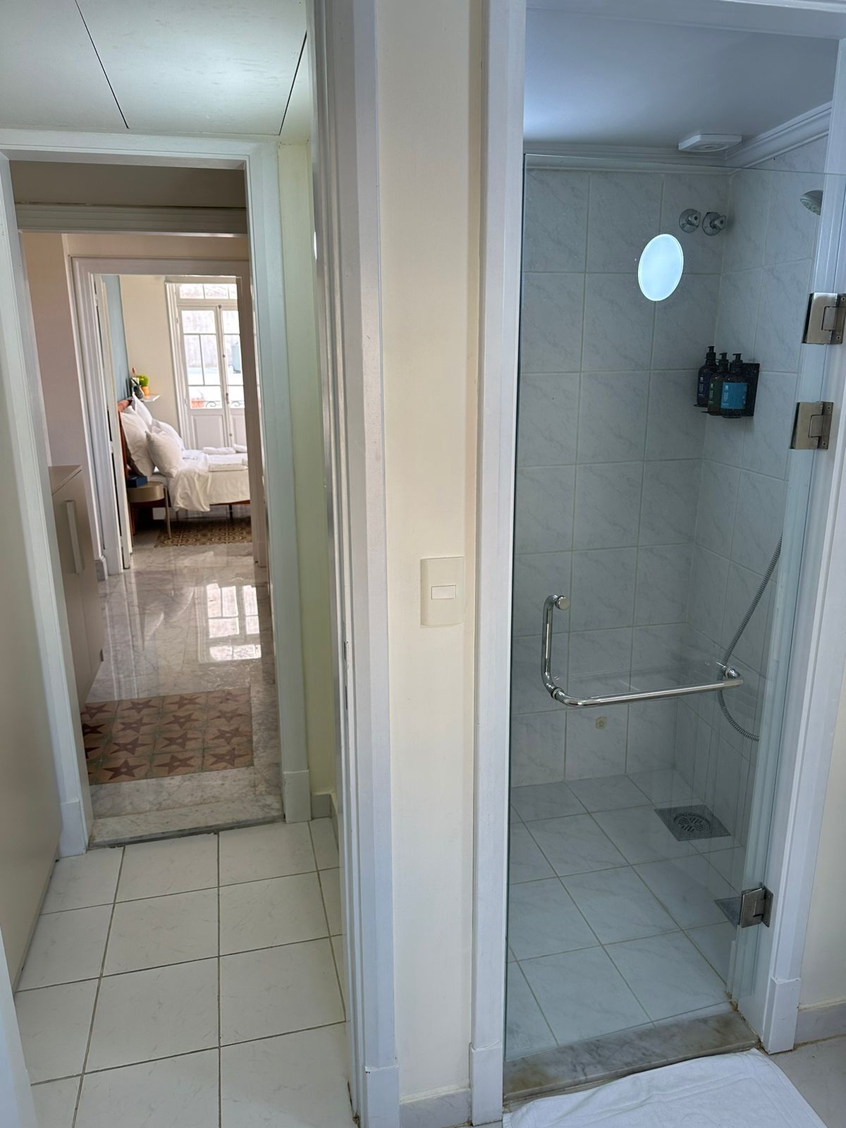 A bathroom with a glass shower enclosure, a handheld showerhead, and a handheld soap dispenser.
