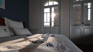 Una cama bien hecha con toallas y una ventana por donde entra la luz del sol.