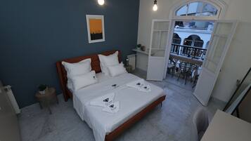 A bedroom with a large bed, two bedside tables, a nightstand, a window with a view, and a balcony with chairs.
