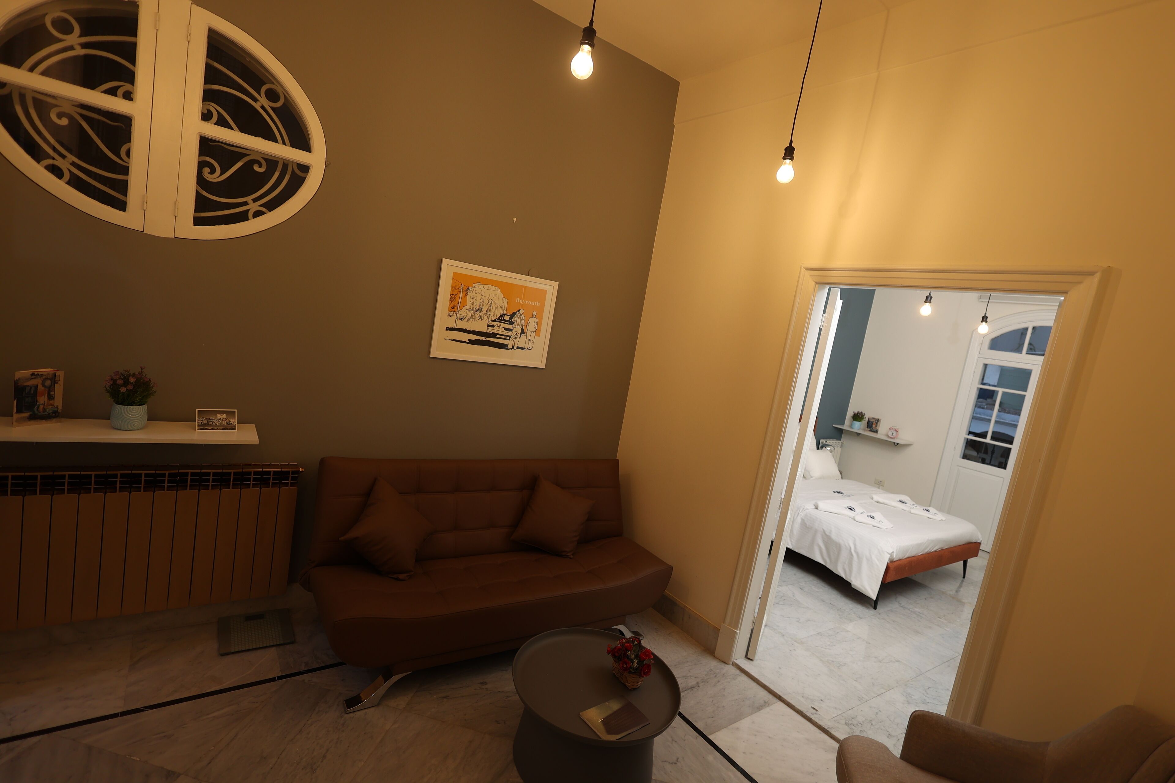 A cozy living room with a brown sofa, a small round table with a vase, and a ceiling light fixture.