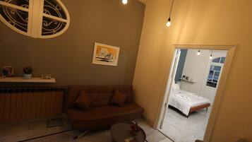 A cozy living room with a brown sofa, a small round table with a vase, and a ceiling light fixture.