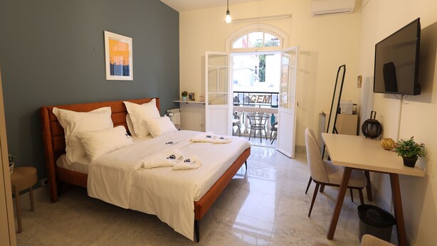 Un dormitorio con cama, mesita de noche y televisión. Cuenta con un balcón con una silla y una mesa.