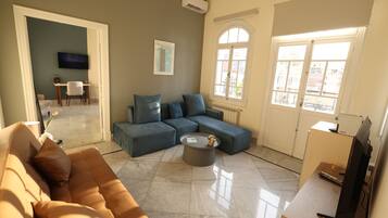 A living room with a sectional sofa, a coffee table, a TV, and a window with a view of buildings.