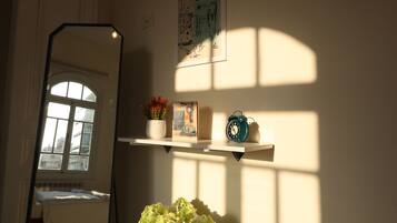 A room with a large mirror, a vase with flowers, a clock, and a shelf with decorative items.