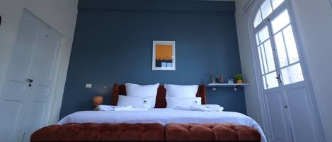 Un dormitorio con una cama grande, una ventana, una puerta y una repisa con una planta.
