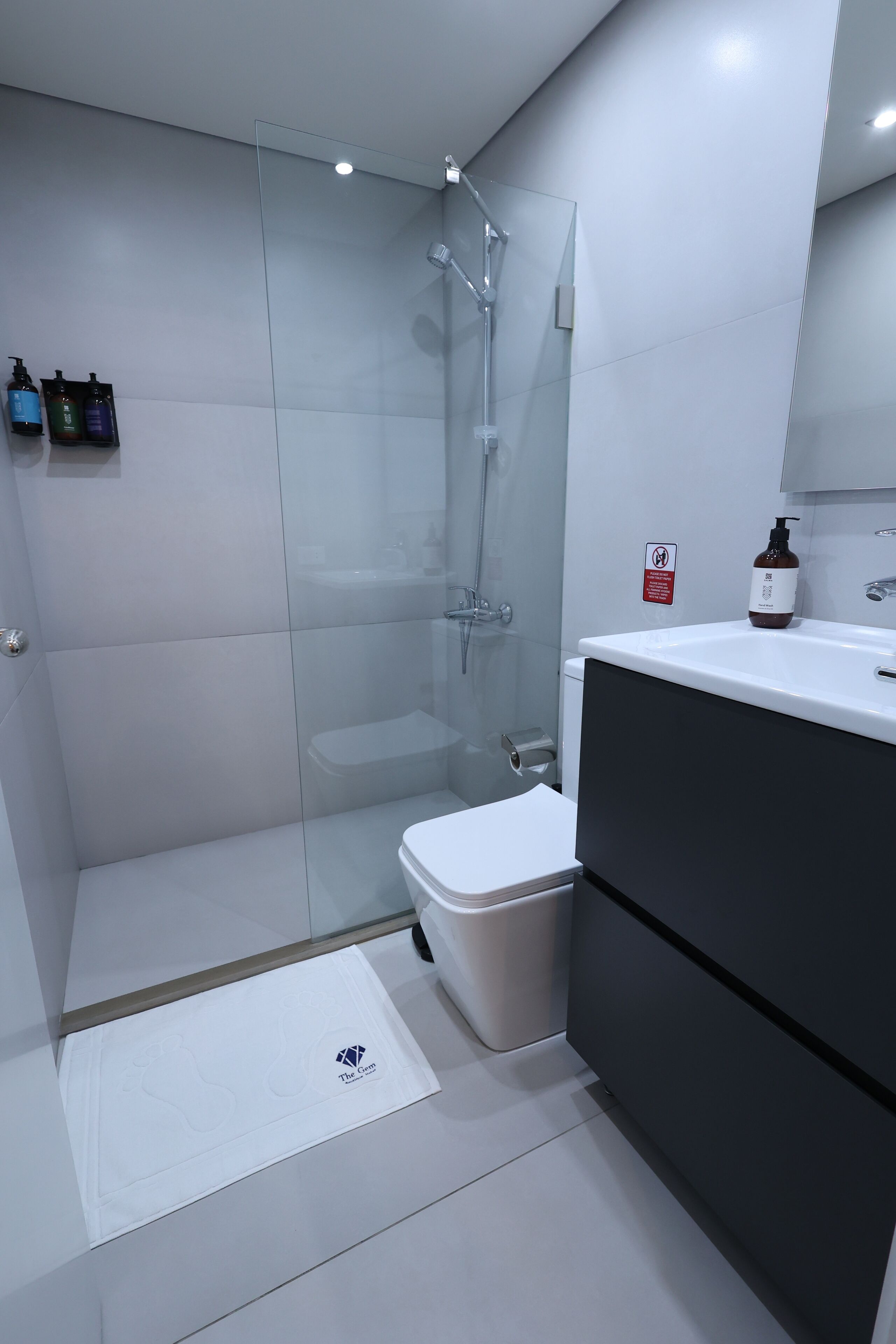 Un baño moderno con cabina de ducha de vidrio, inodoro blanco y tocador oscuro con espejo.