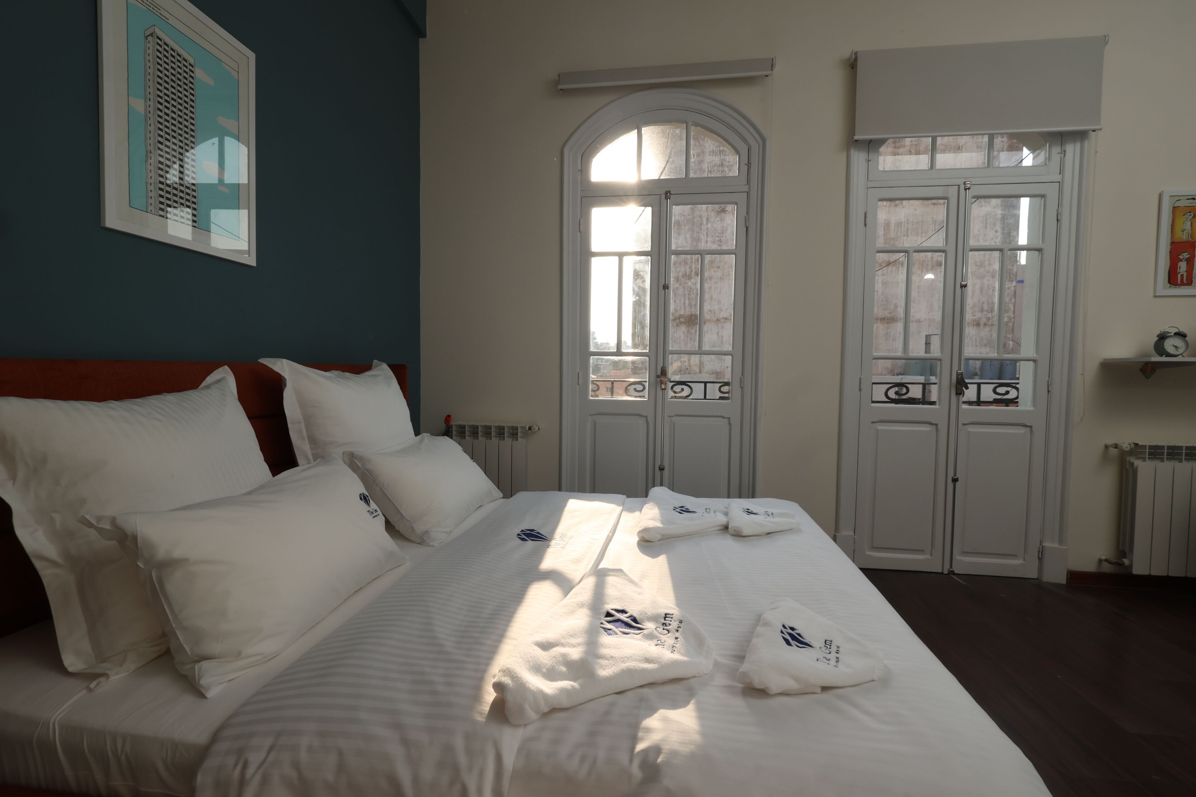 A hotel room with a bed, white linens, a window with a view, and a door with a radiator.