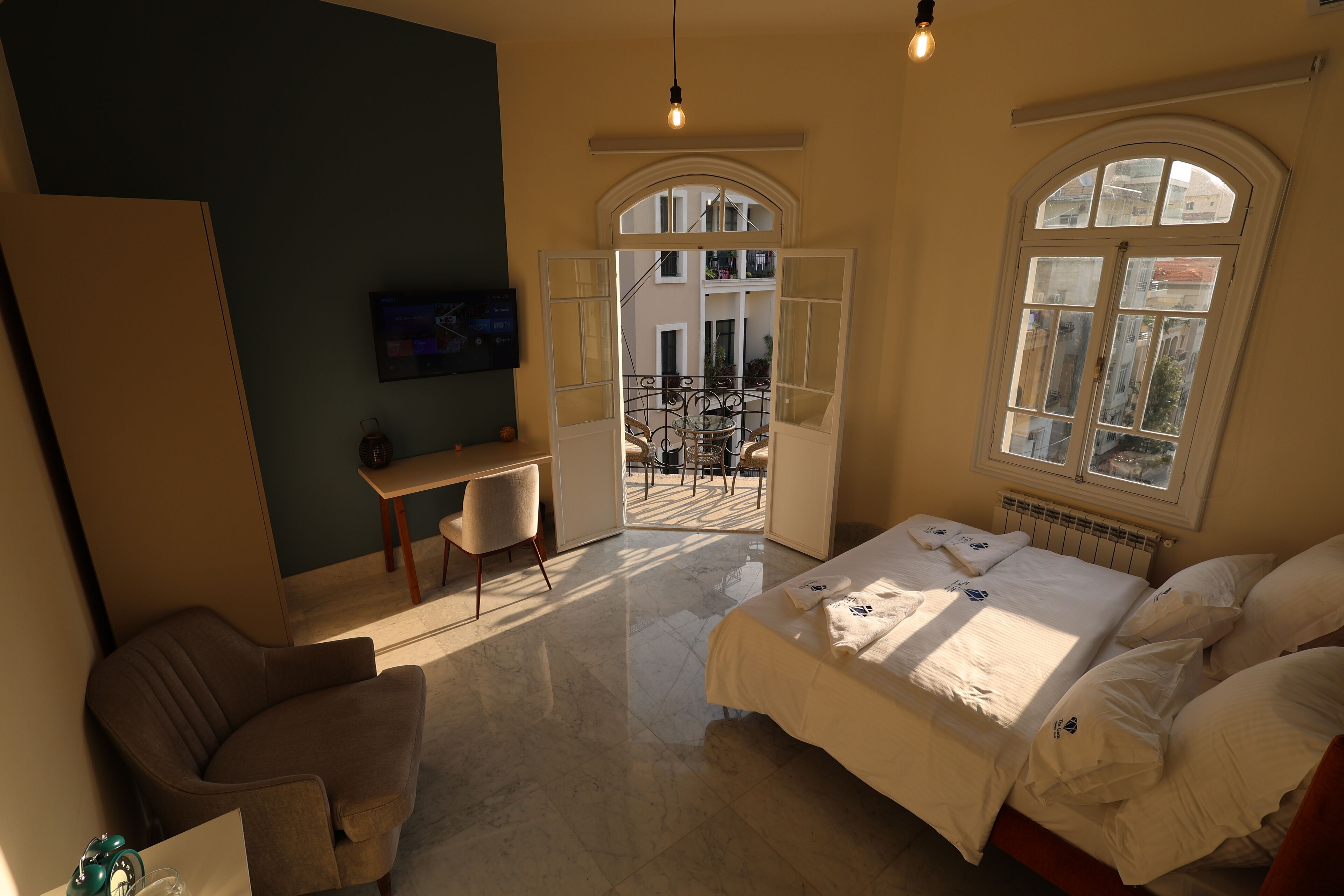 A hotel room with a bed, a desk, a chair, and a view of the outside balcony.