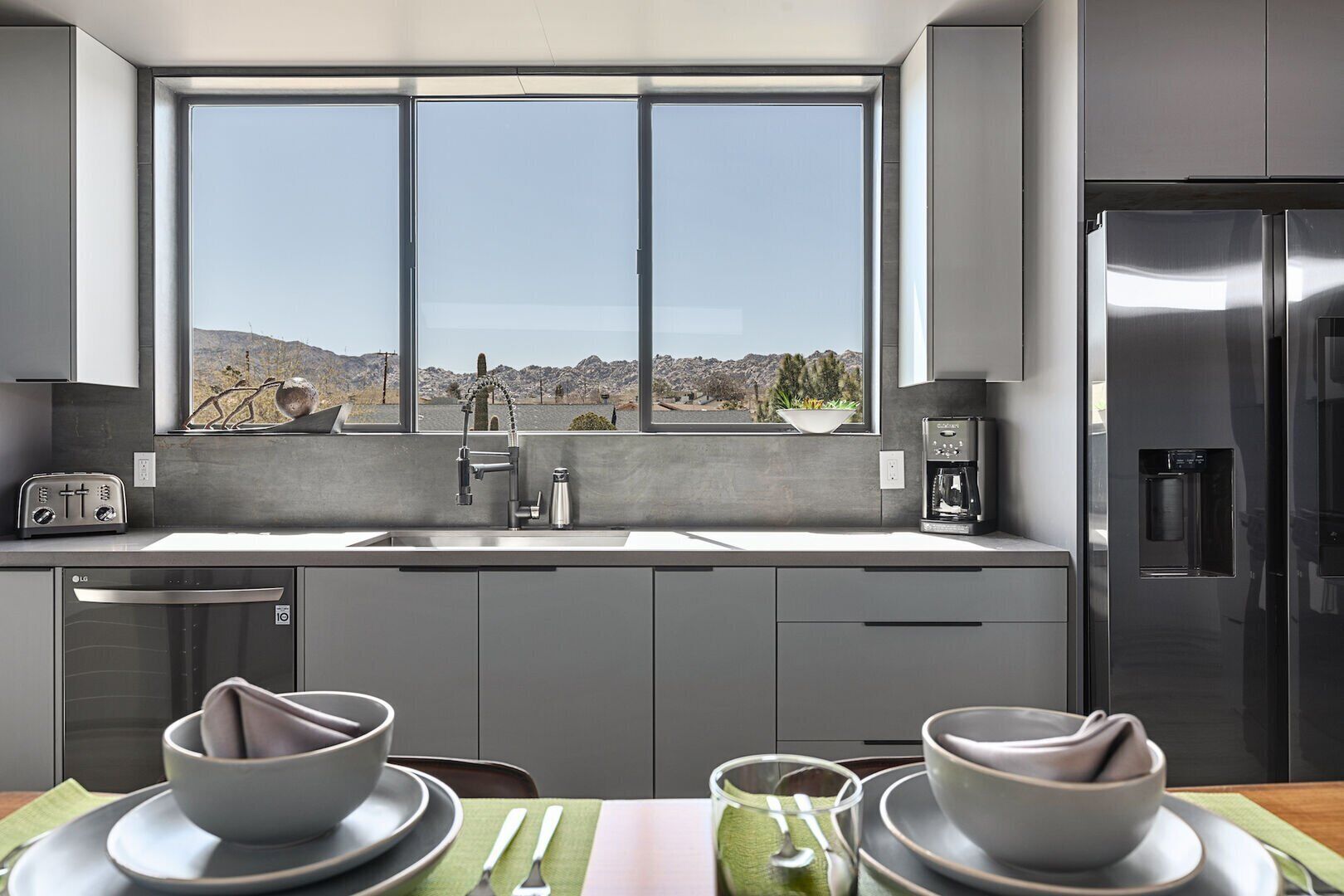 Una cucina moderna con un'ampia finestra, elettrodomestici in acciaio inox e vista su un paesaggio roccioso.