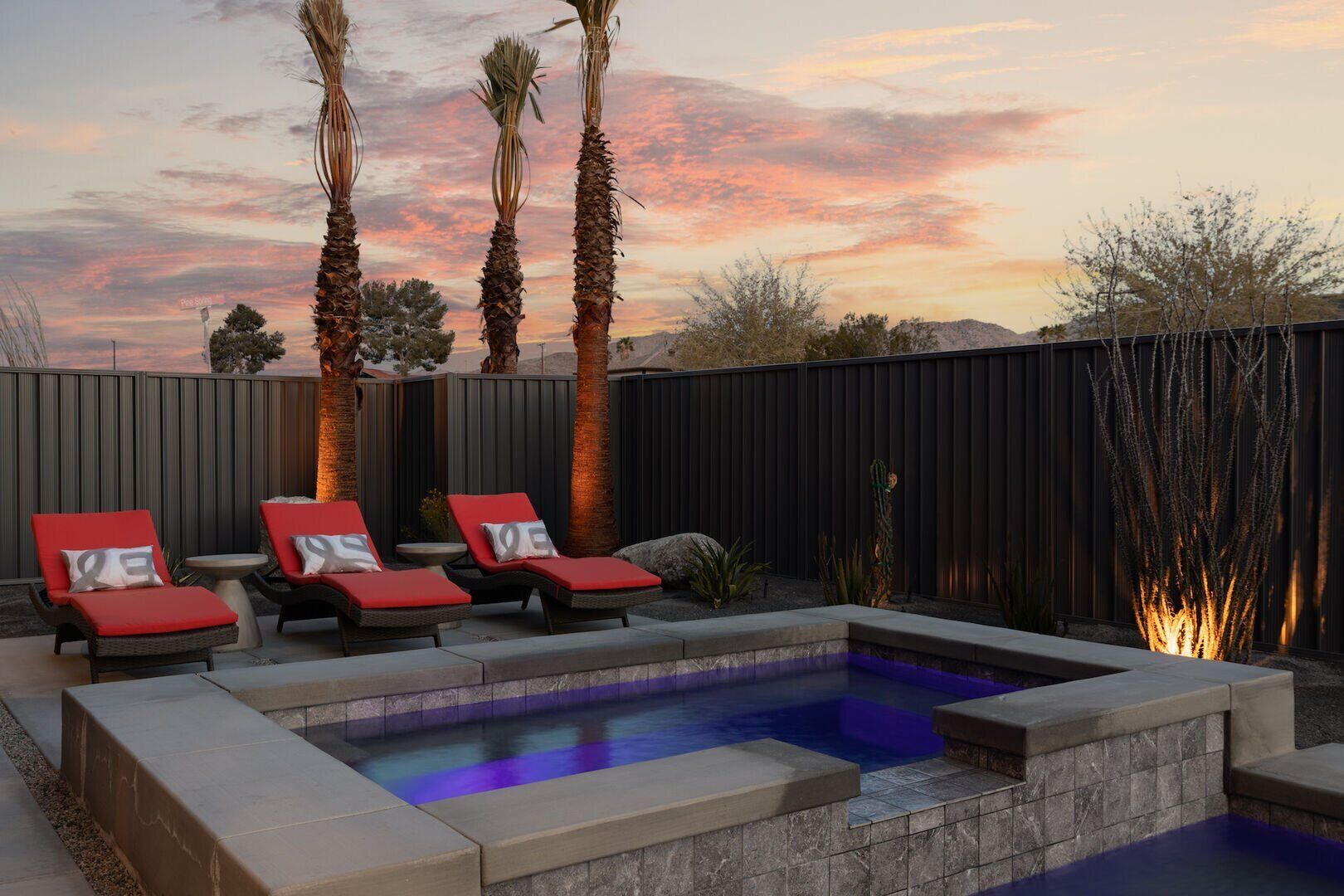 A backyard with a swimming pool, red lounge chairs, and a wooden fence.