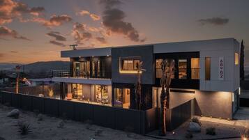 A modern two-story house with a balcony, large windows, and a desert landscape.