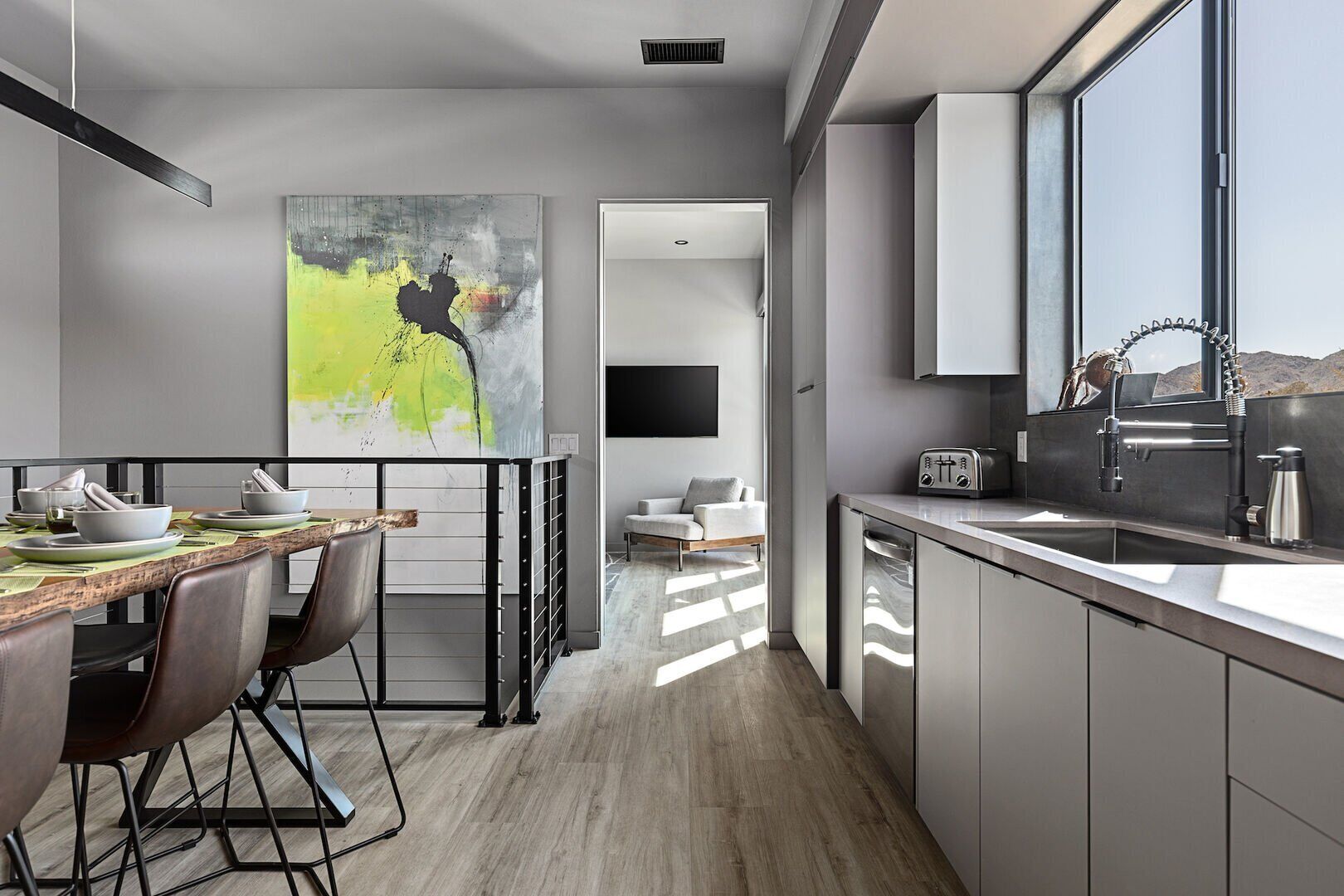 A modern kitchen with a dining area, a large abstract painting, and a view of the outdoors.