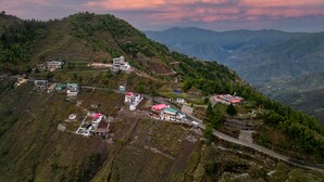 A mountainous village with terraced fields, buildings with red roofs, and a winding road. - Le Masrana Inn (Dehradun)
