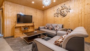 A wooden-paneled room with a sofa, a coffee table, a flat-screen TV, and a decorative wall piece. - Le Masrana Inn (Dehradun)
