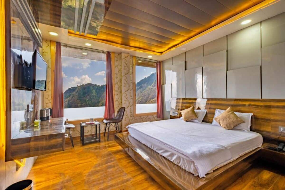 A modern hotel room with a large bed, a desk with a chair, a TV, and a view of mountains.