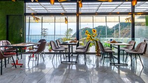 A modern dining area with a glass ceiling, large windows, and a view of a mountainous landscape. - Le Masrana Inn (Dehradun)