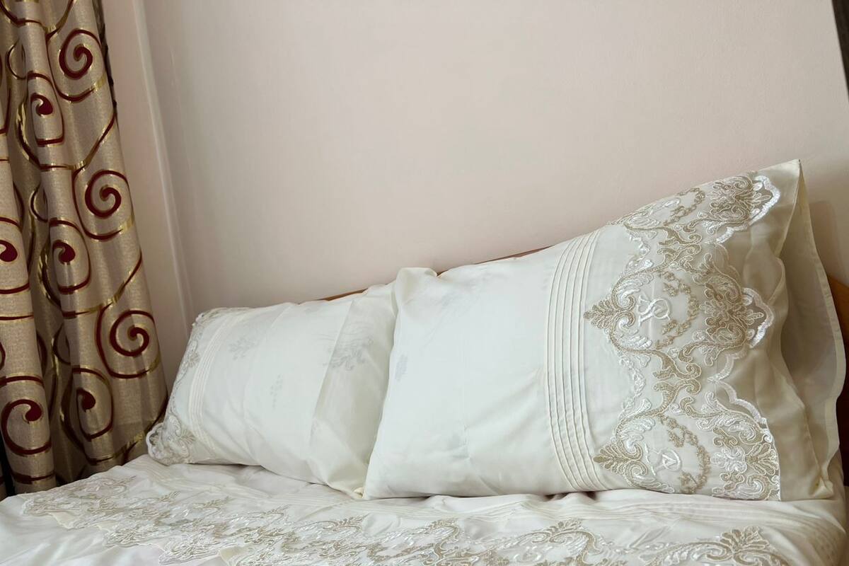 A bed with white linens and decorative pillows, a curtain with a swirl pattern, and a plain wall.