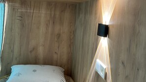 Ein Zimmer mit Holzboden, einem Bett, einer Wandleuchte und einem Fenster mit Vorhängen.