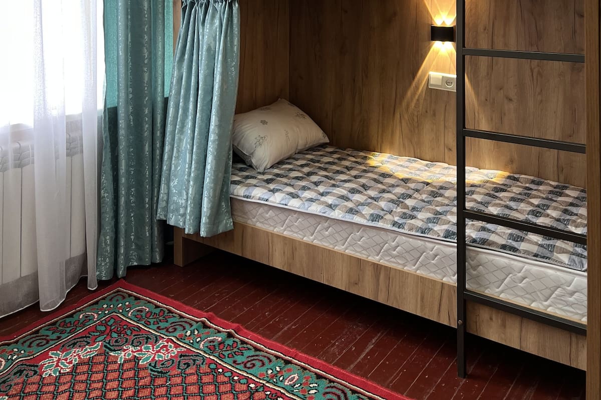 A bunk bed room with wooden walls, a red patterned rug, and a window with sheer curtains.