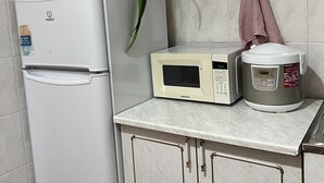 Eine Küche mit einem weißen Kühlschrank, einer Mikrowelle und einem Reiskocher auf der Arbeitsfläche.