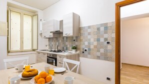 A modern kitchen with white cabinets, a tiled backsplash, and a dining area with a table set for breakfast. - Central Station Family Apt by Wonderful Italy (Naples)