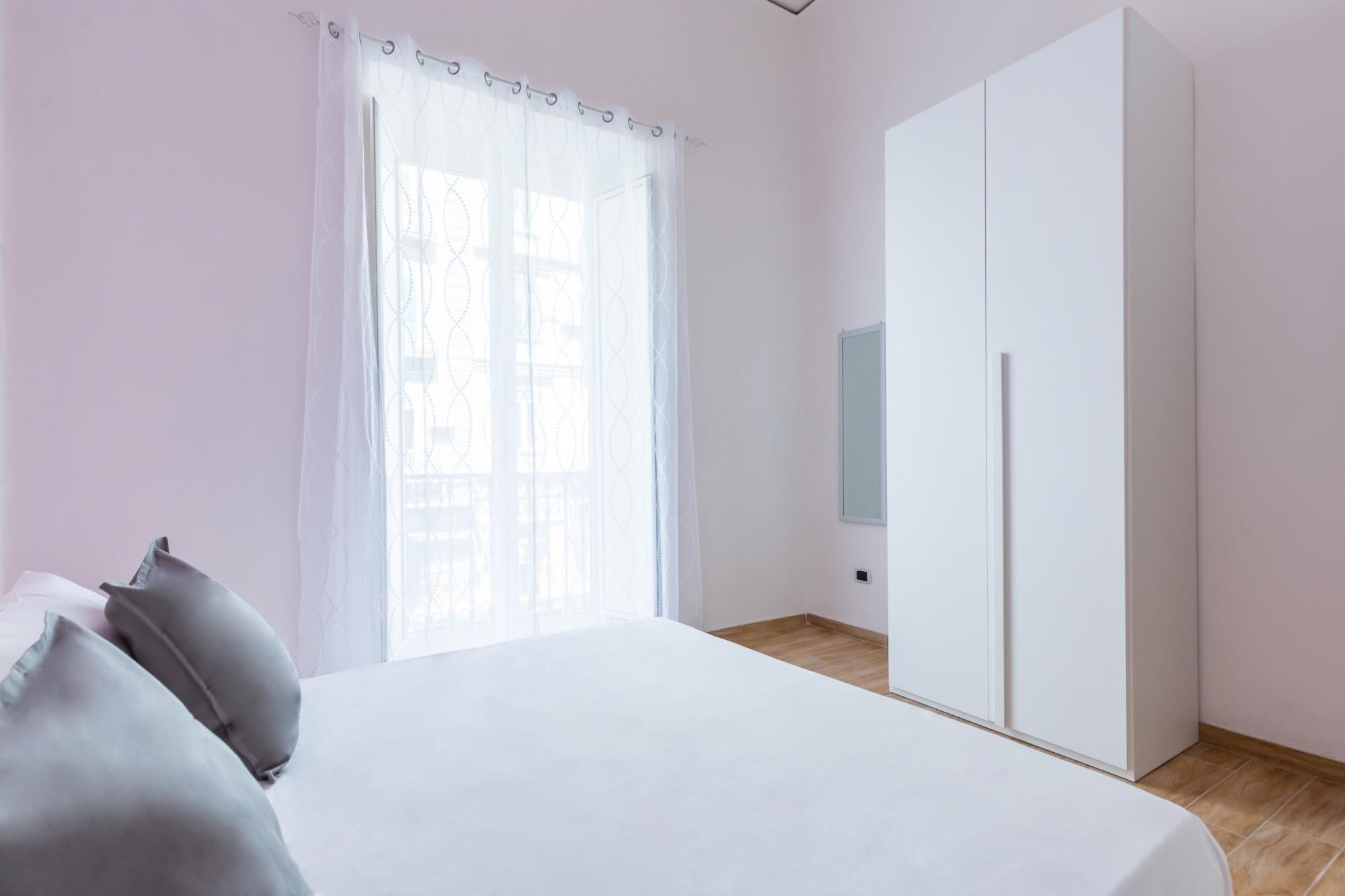 Un dormitorio con cama, armario y ventana con cortinas traslúcidas.