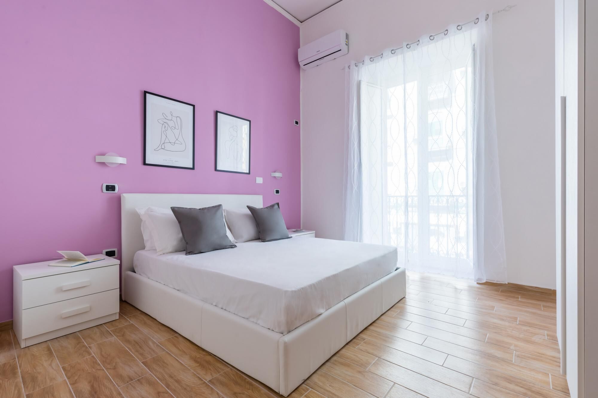 Ein Schlafzimmer mit einem Bett, einem Nachttisch, Vorhängen an einem Fenster und einer Wand-Klimaanlage.