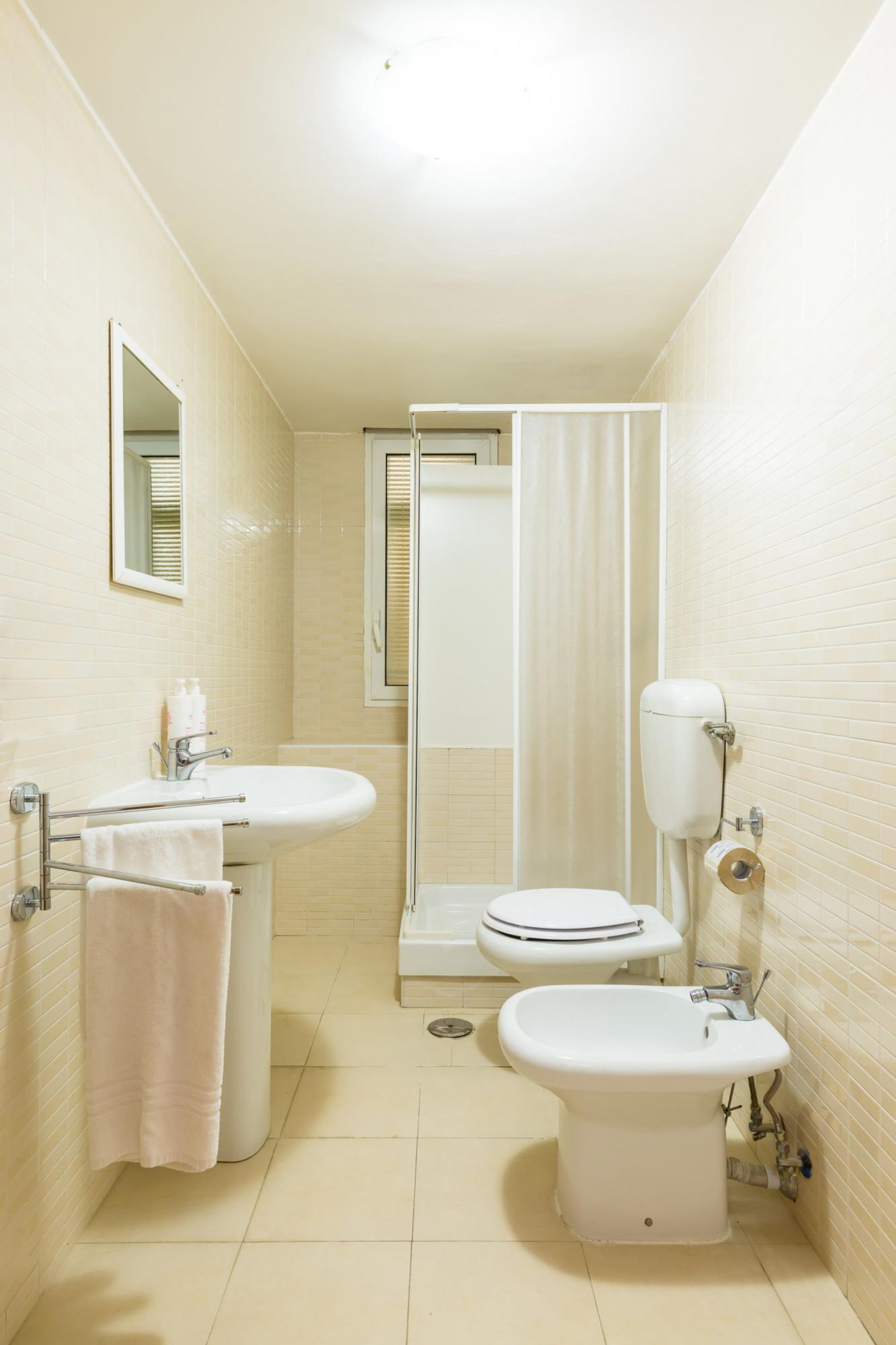 A small, clean bathroom with a sink, toilet, bidet, and shower curtain.