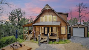 A wooden cabin with a porch, a covered deck, and a garage. - Luxury 2 Bedroom Cabin with Hot Tub, Pool Table, Resort Amenities and More! (Sevierville)