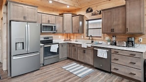 A modern kitchen with wooden cabinets, stainless steel appliances, and a granite countertop. - Luxury 2 Bedroom Cabin with Hot Tub, Pool Table, Resort Amenities and More! (Sevierville)