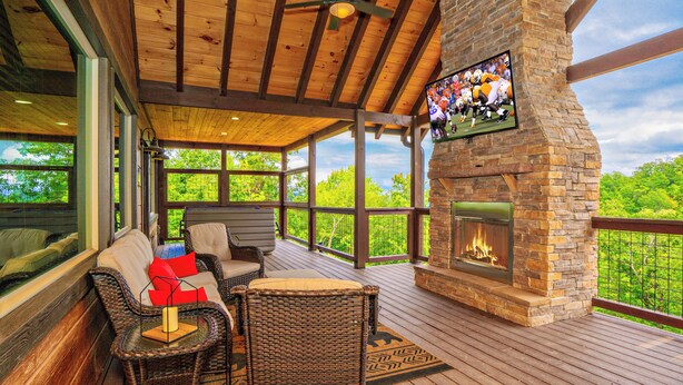 A covered outdoor deck with wicker furniture, a stone fireplace, and a TV mounted on the wall. - ALongViewSplash: Pool, Mtn View, Pet-Friendly, Theater, Game Room, Hot Tub, WiFi (Sevierville)