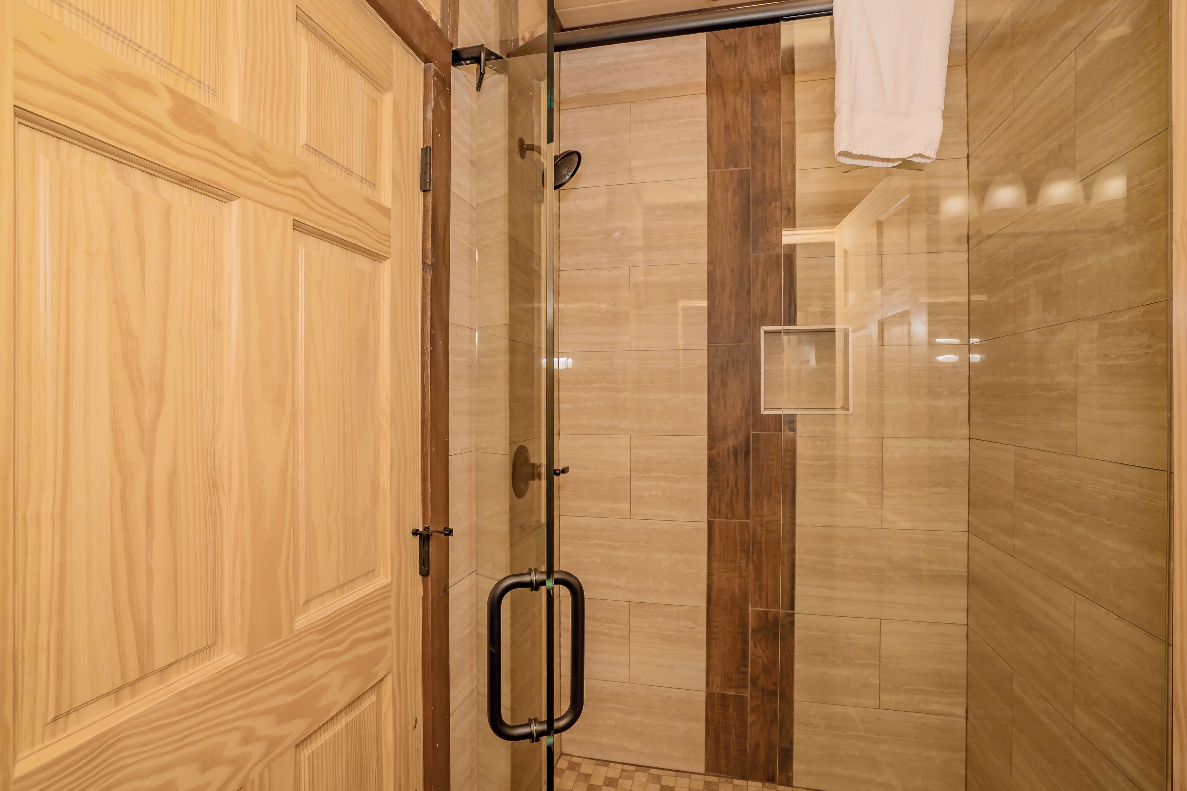 A shower area with a glass door, wooden paneling, and a tiled floor.