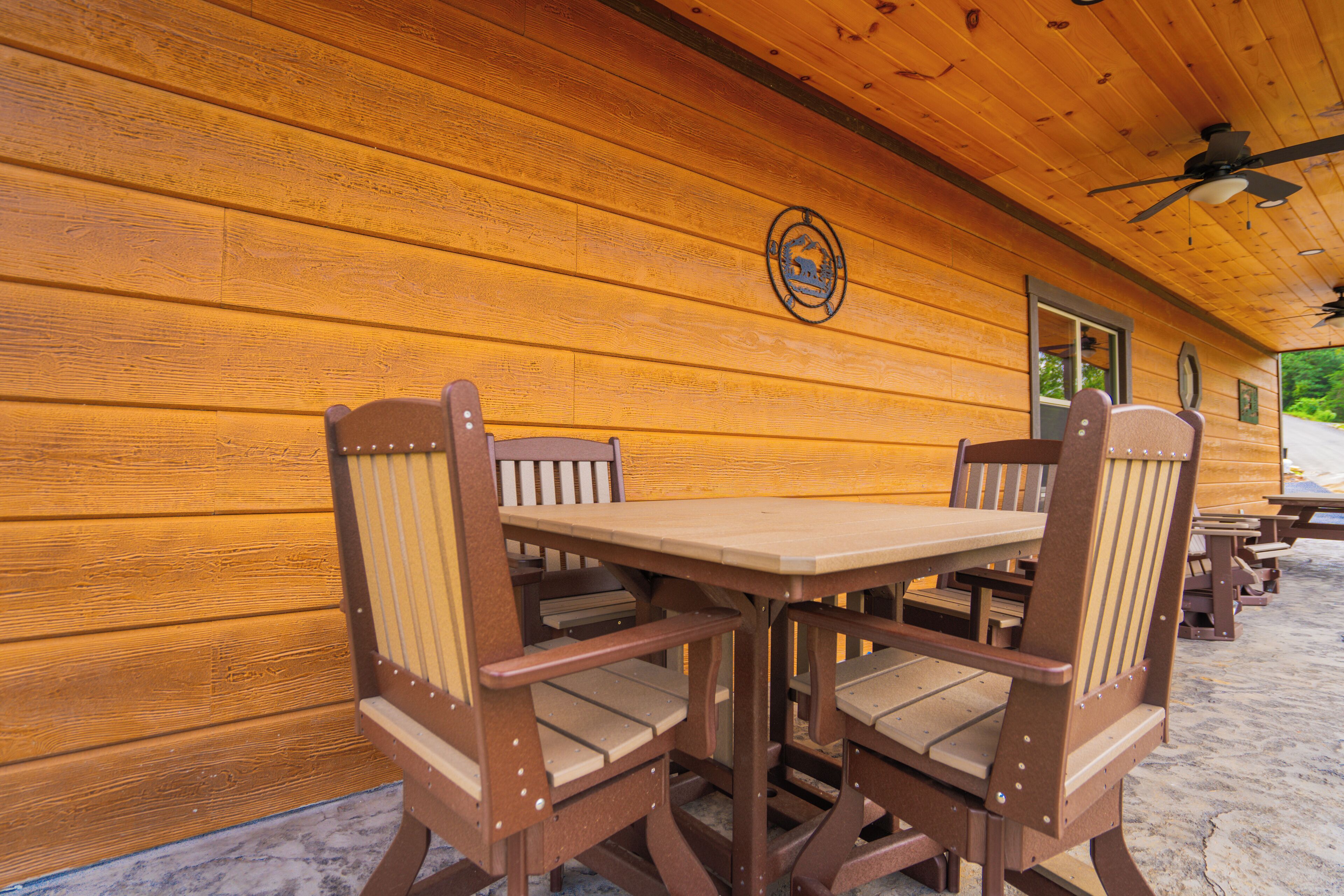 A covered patio area with wooden benches and tables, a ceiling fan, and a wooden wall with a logo.