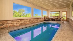 An indoor swimming pool with stone walls, large windows, and wooden chairs. - ALongViewSplash: Pool, Mtn View, Pet-Friendly, Theater, Game Room, Hot Tub, WiFi (Sevierville)