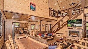 A spacious wooden interior with a dining area, fireplace, and a staircase leading to an upper level. - ALongViewSplash: Pool, Mtn View, Pet-Friendly, Theater, Game Room, Hot Tub, WiFi (Sevierville)