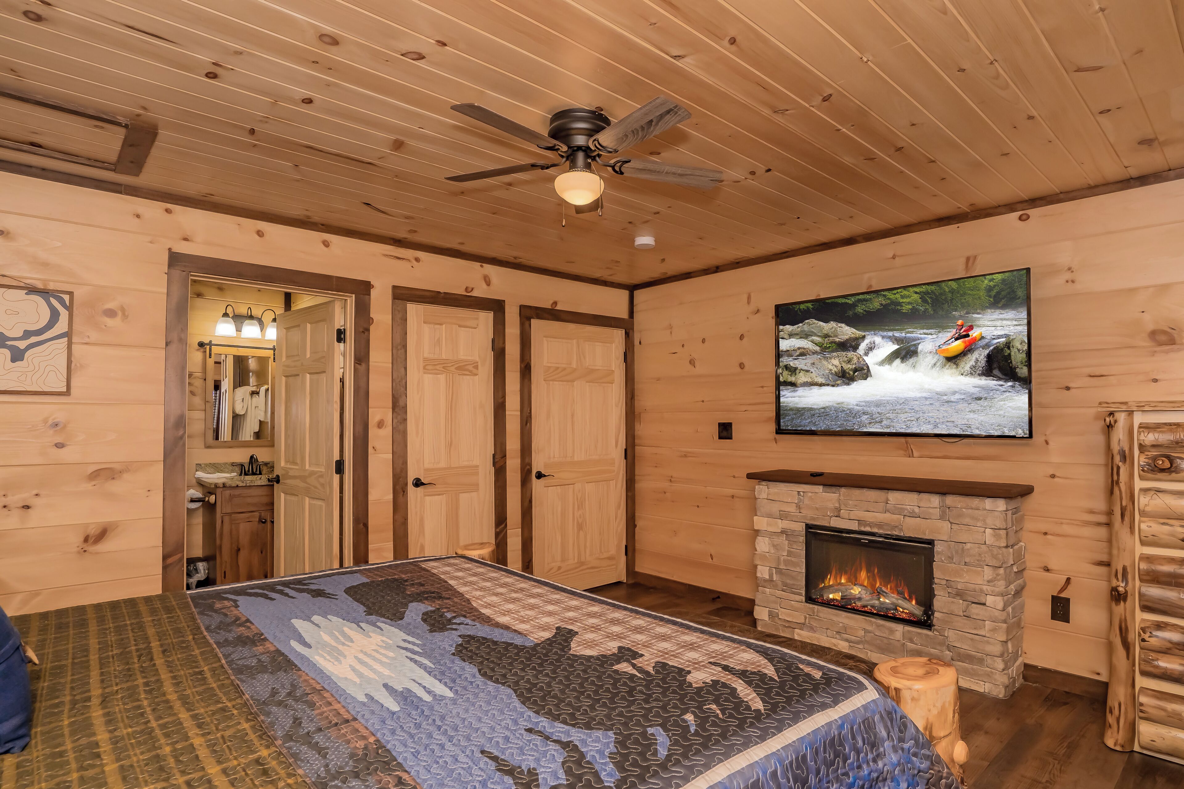 A log cabin room with a bed, a fireplace, a television, and a ceiling fan.