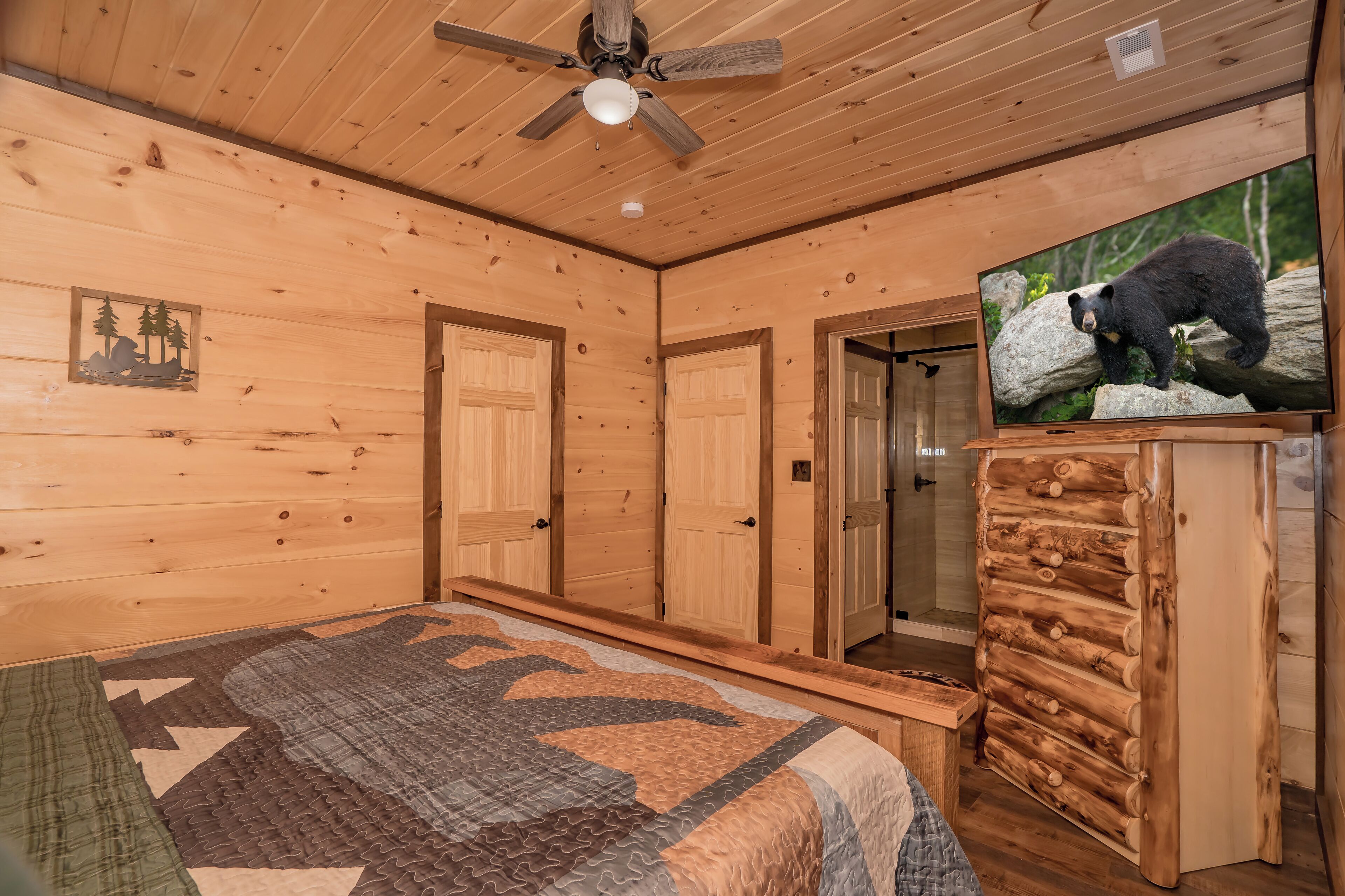 A wooden cabin room with a bed, a television displaying a bear, and a ceiling fan.