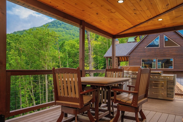 A wooden deck with a table and chairs, overlooking a forested mountain.