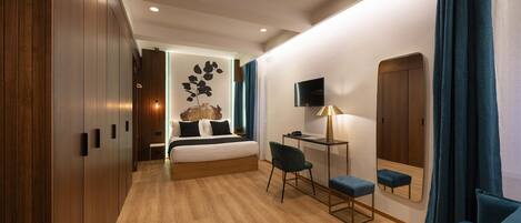 Une chambre d’hôtel moderne avec un plancher en bois, un lit avec une tête de lit, un bureau avec une chaise, une télévision et un miroir.