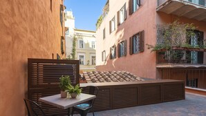 A small outdoor seating area with a table and chairs, surrounded by buildings with balconies and windows. - Palazzetto Symphony (Rome)