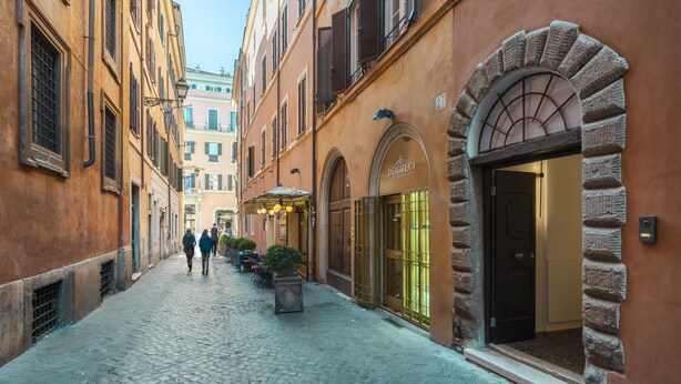 A cobblestone street with historic buildings, a shop with a sign 'DEIGRECCI', and a stone archway. - Palazzetto Symphony (Rome)