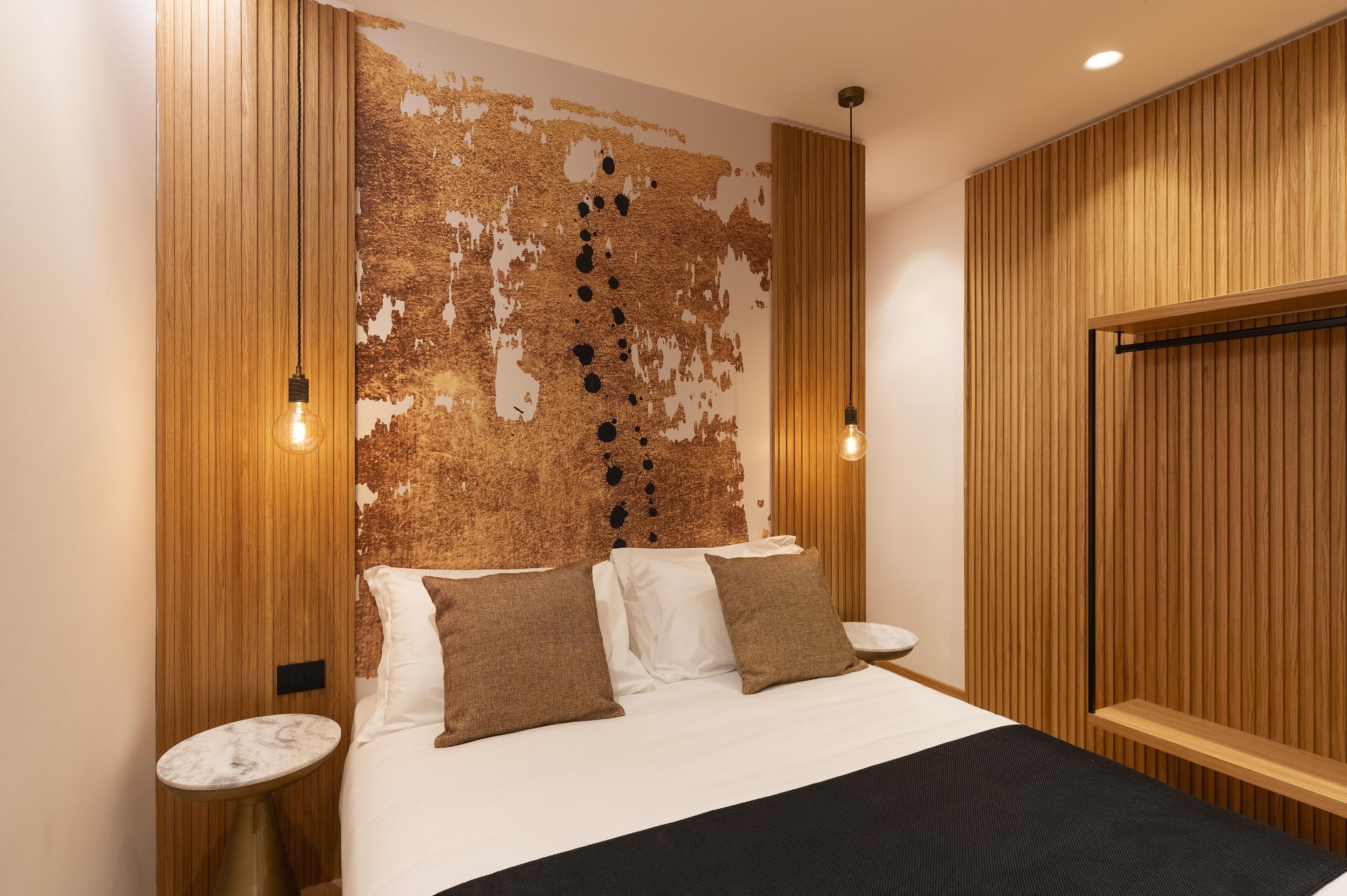 Une chambre d’hôtel moderne avec un grand lit, des panneaux de bois et deux lampes fixées au mur.