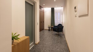 A hallway with a wooden console, a potted plant, a blue chair, and a small table with a plant. - Palazzetto Symphony (Rome)