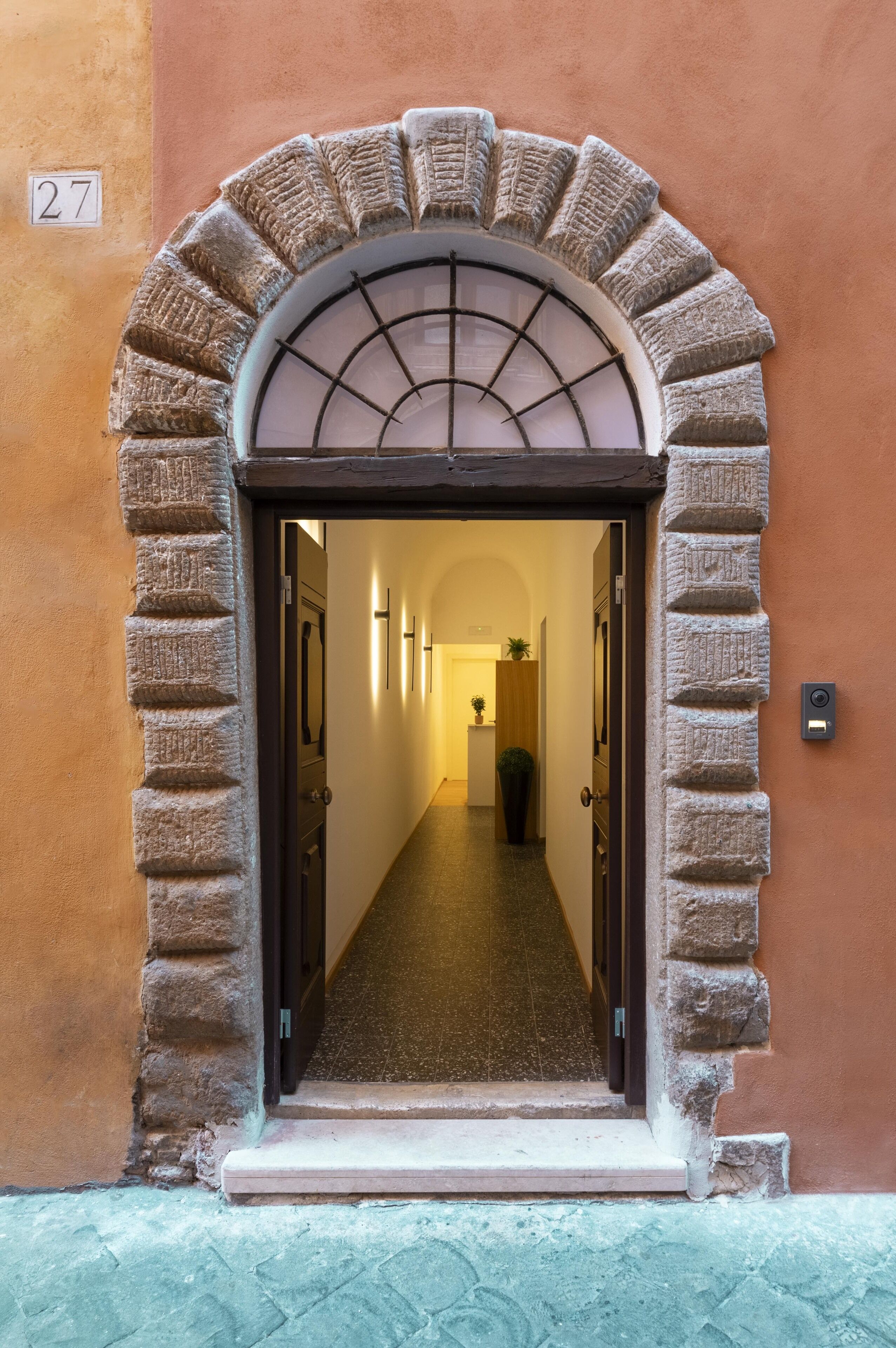 Un arco de entrada que da a un pasillo con suelo de baldosas y un cartel con el número 27.