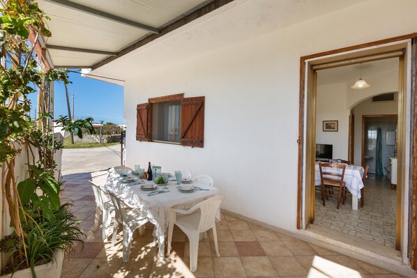 Un comedor con una mesa dispuesta para dos, una ventana con contraventanas de madera y vistas a la calle.